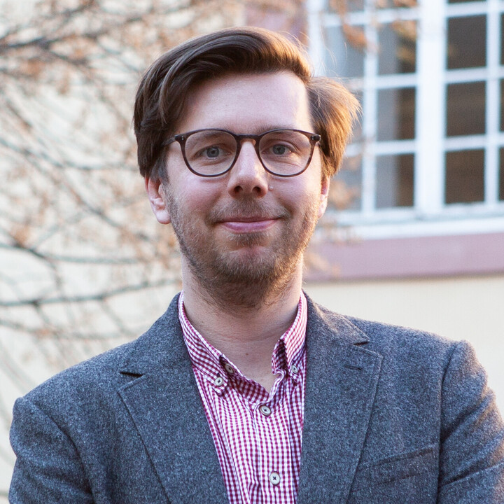 Prof. Dr. Dörrenberg mit braunen Haaren, brauner Brille, rot-weiß-kariertem Hemd und grauem Sakko im Schlossinnenhof