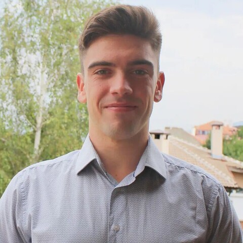 Georgi Paskalev hat kurze braune Haare und trägtein graues Hemd. Im Hintergrund sieht man ein paar Bäume und Häuser.