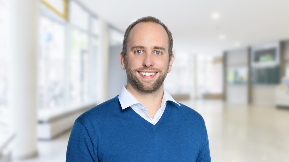 Portrait von Sebastian Siegloch. Er trägt einen blauen Pullover.