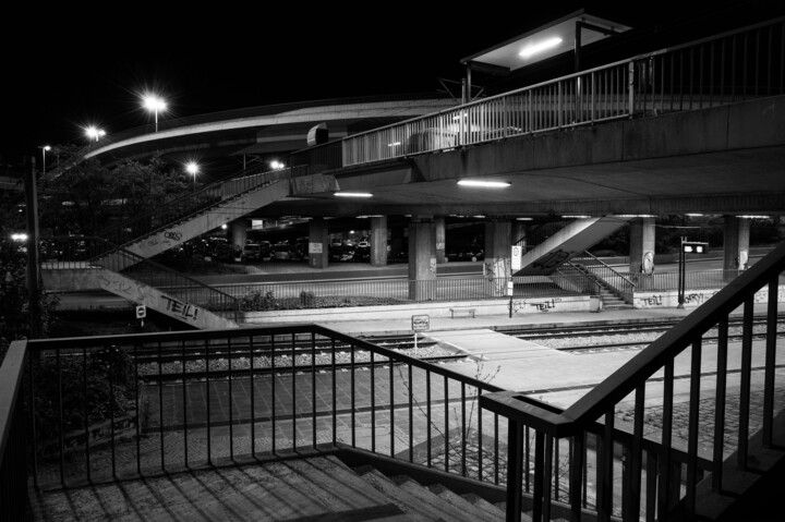 Schwarzweißfoto der Haltestelle "Rheinstraße". Blick von der Seite auf die Brücke, unter der sich die Gleise befinden.