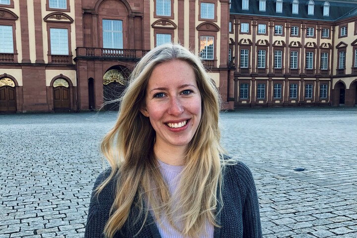 Alicia Minnerup hat lange blonde Haare und trägt einen rosa Pullover und einen dunkelgrauen Cardigan. Im Hintergrund ist das Schloss zu sehen.