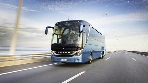 Ein Mann mit Sonnenbrille fährt einen blauen Reisebus auf einer nicht befahrenen Autobahn.