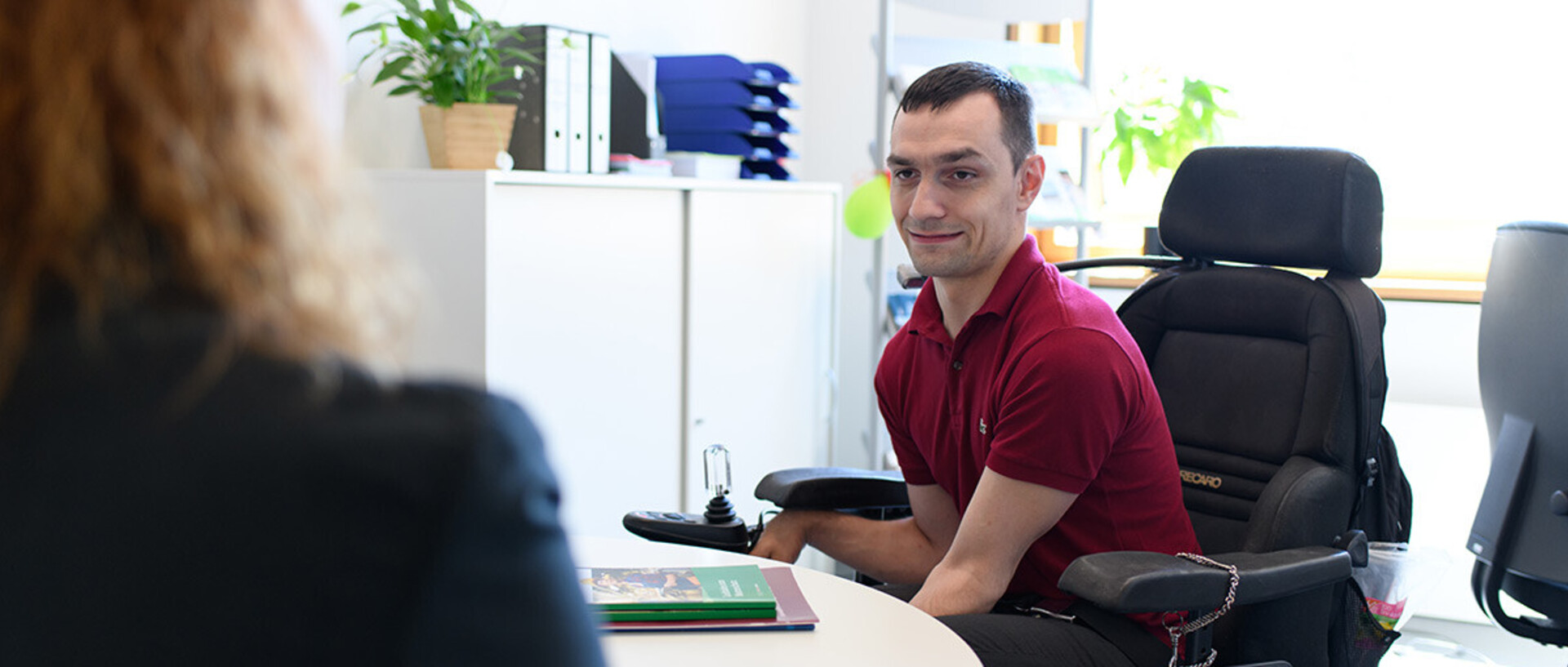 Eine Mitarbeiterin berät einen Studenten, der im Rollstuhl sitzt.