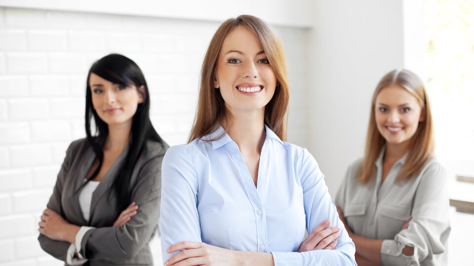 Drei lächelnde Frauen in Businesskleidung und mit verschränkten Armen