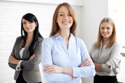 Drei lächelnde Frauen in Businesskleidung und mit verschränkten Armen