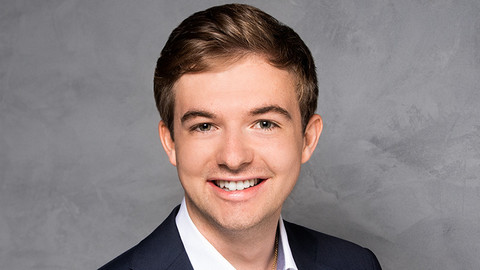 Frederik Kohl. He is wearing a dark jacket over a white shirt and is standing in front of a grey wall.