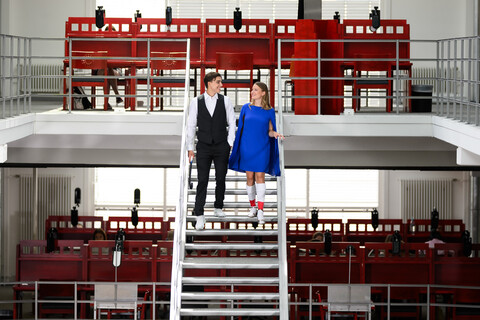 Ein Feldhockeyspieler und eine Feldhockeyspielerin in formaler Kleidung gehen die Treppe in der A3 Bibliothek hinunter.