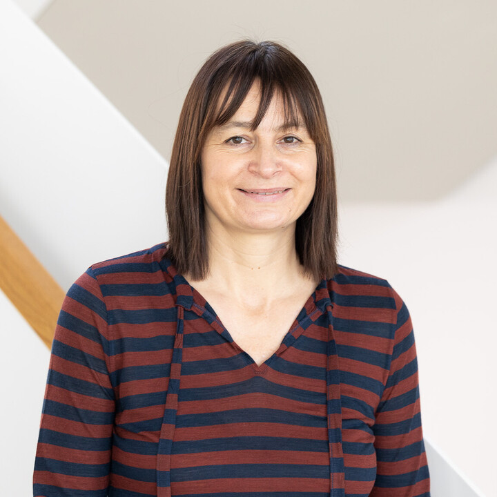 Carola Trips vor einem hellen Hintergrund. Sie trägt ein braun-blau gestreiftes Kapuzenoberteil.