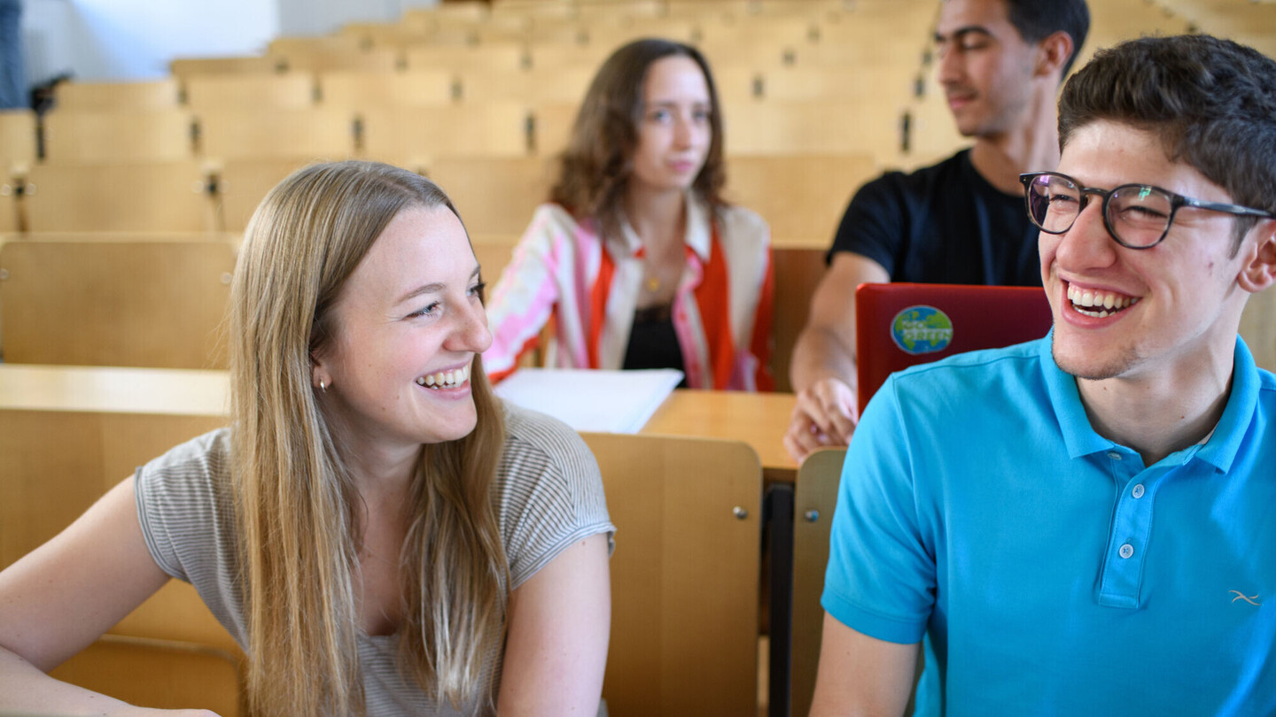 Studierende sitzen lachend in einem Vorlesungsraum 