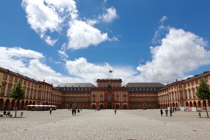 Das sandsteinfarbene Mannheimer Barockschloss mit Blick auf den Mittelbau bei strahlend blauem Himmel. Vereinzelt schlendern junge Menschen über das Kopfsteinpflaster auf dem Ehrenhof.