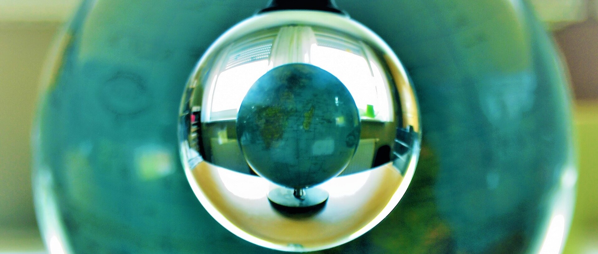 In einer silbernen Glühbirne spiegelt sich ein Globus, der auf einem Schreibtisch vor dem Fenster steht