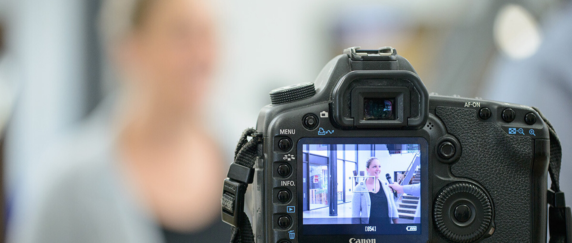 Auf der Bildanzeige einer Digitalkamera ist das Bild einer Frau zu sehen, die mit einem Mikrofon interviewt wird.