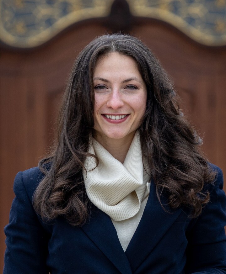 Portrait von Giuliana Manganaro. Sie steht auf dem leicht windigen Ehrenhof und trägt ein blaues Jackett über einem beigen Rollkragenpulli.