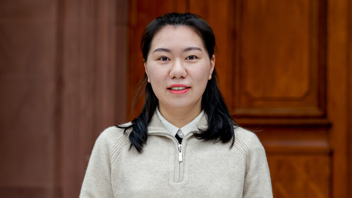 Portrait of Siyu Zhang. She is wearing an off-white sweater and is standing in front of a door of Mannheim Palace.