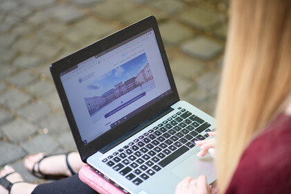 Eine Frau sitzt auf einem Steinboden und hat ihren Laptop auf dem Schoß.