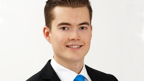 Jan Schilpp. He is wearing a black suit with a blue tie and is standing in front of a white background.