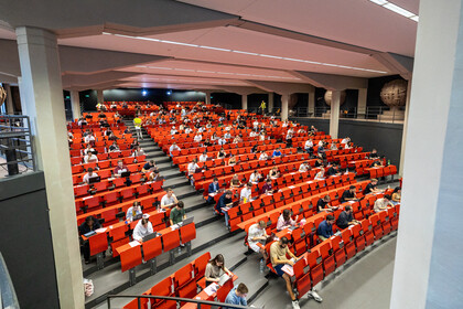 Studierende schreiben eine digitale Prüfung mit Laptops in einem großen Hörsaal mit roten Sitzreihen unter Aufsicht.