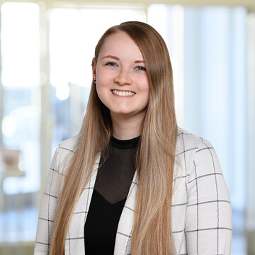 Jessica Scholich hat lange dunkelblonde Haare. Sie trägt einen weißen karierten Blazer und ein schwarzes Oberteil.