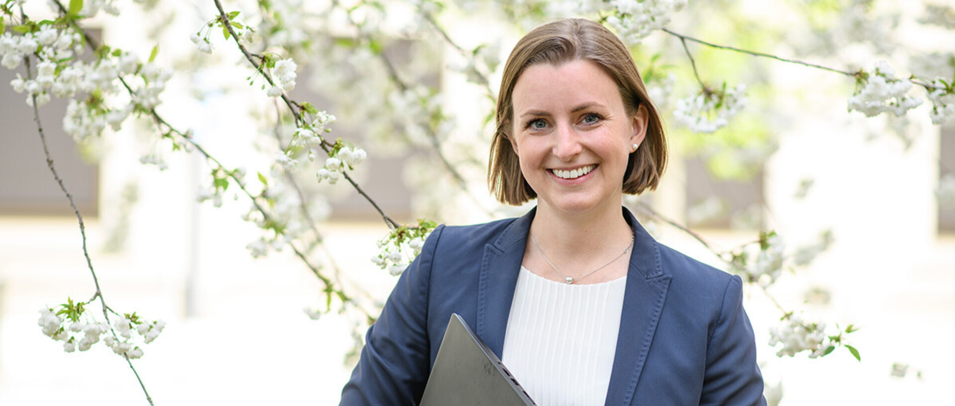 A doctoral student is standing smiling in the courtyard of B6,30-32.