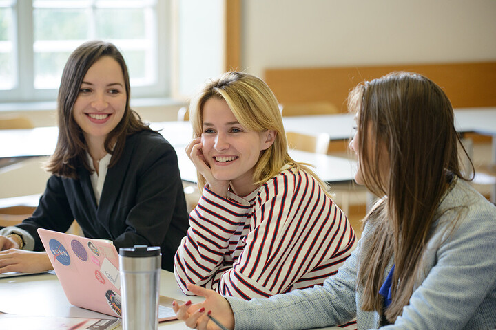 Three female students sit laughing in a seminar room.