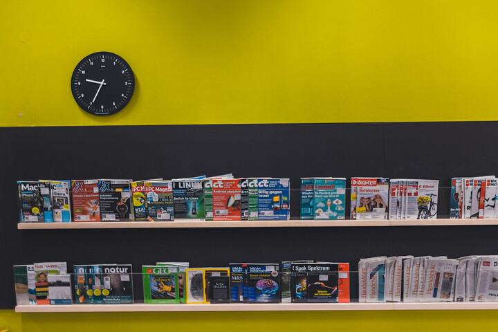 Zwei lange waagrechte Regale, auf denen Zeitschriften aufgestellt sind. Die Zeitschriftencover zeigen nach vorne.