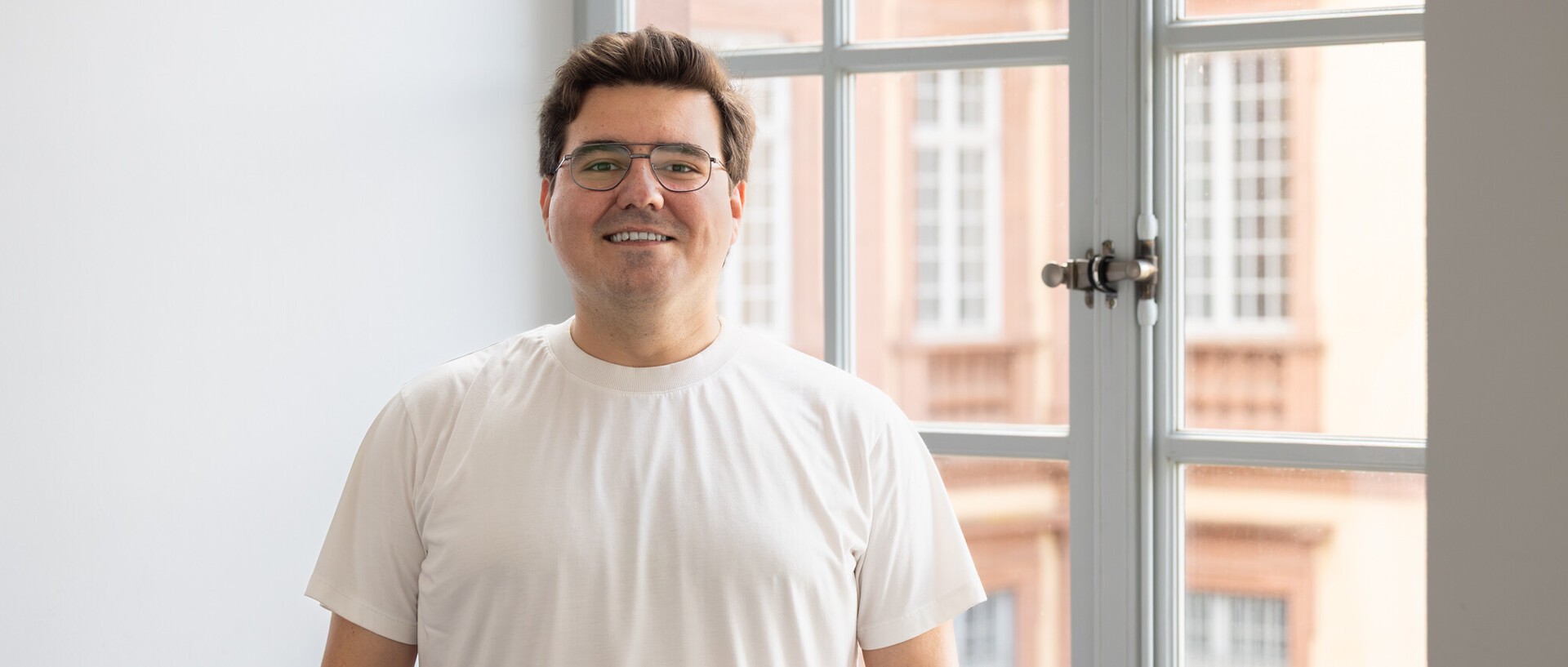 Ayhan trägt ein weißes T-Shirt und eine Brille.
