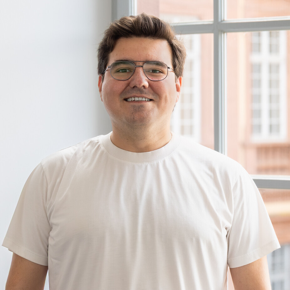 Ayhan trägt ein weißes T-Shirt und eine Brille.