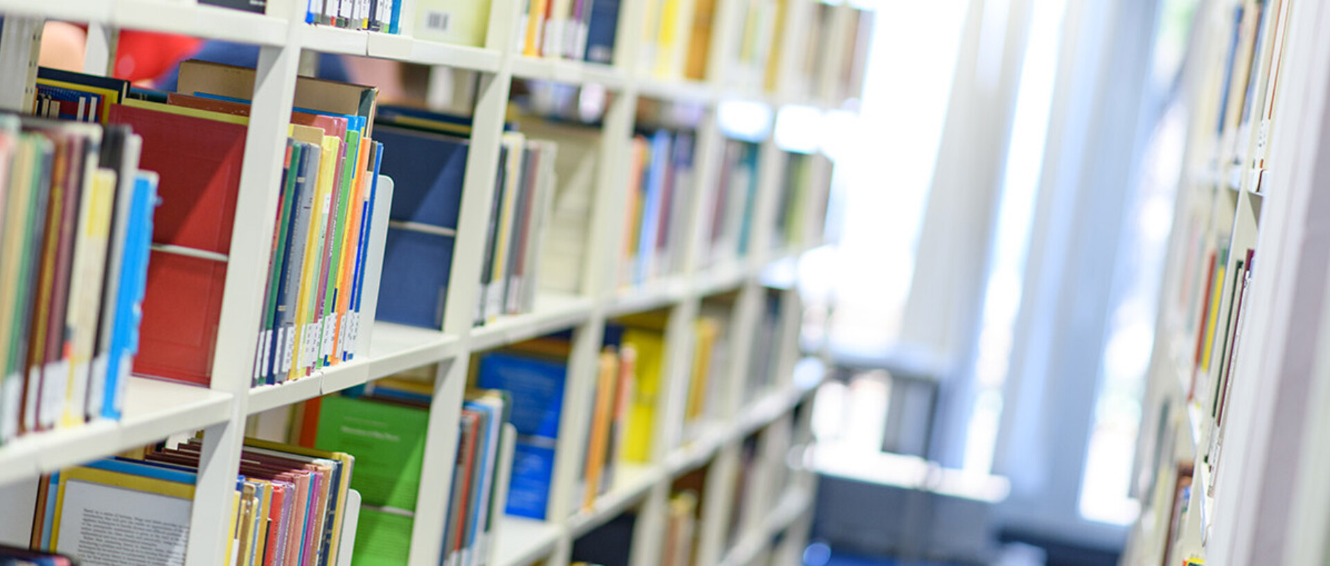 Helle Bibliothekregale mit vielen bunten Büchern.