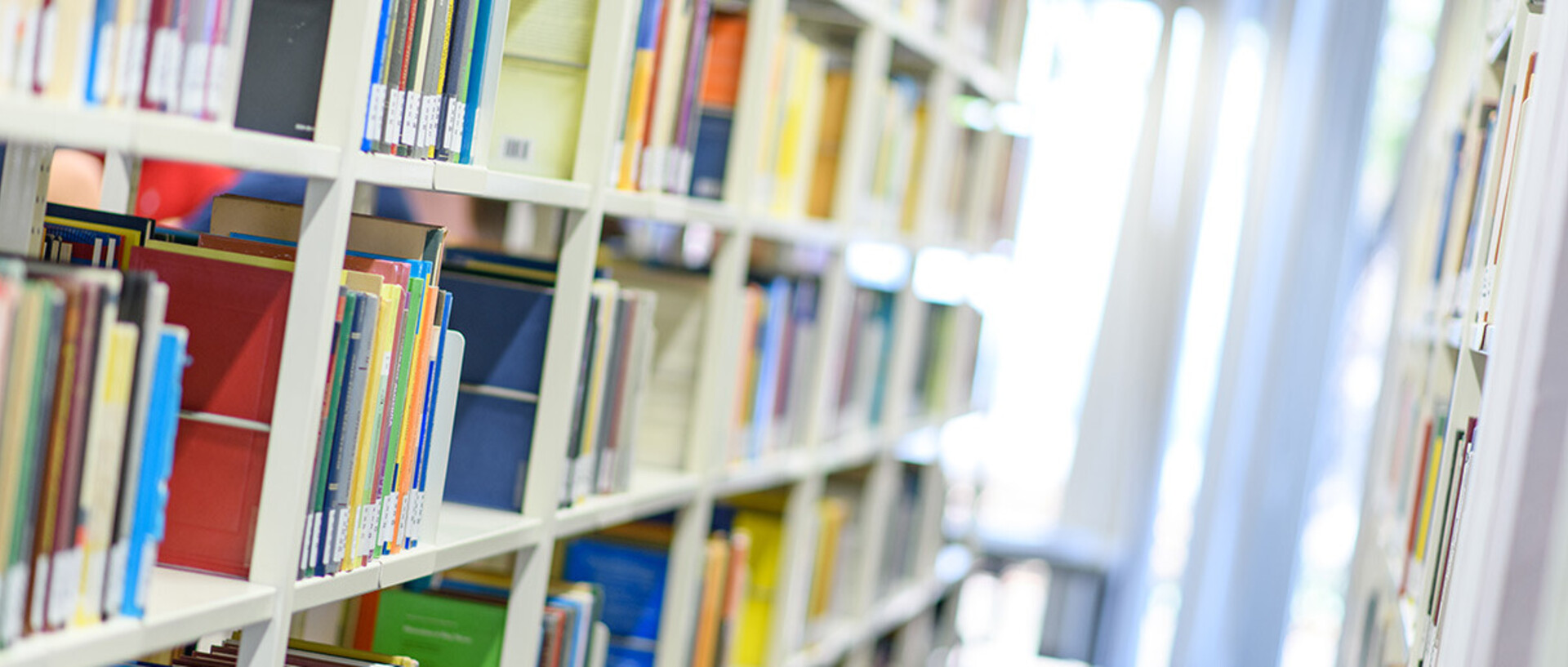Helle Bibliothekregale mit vielen bunten Büchern.