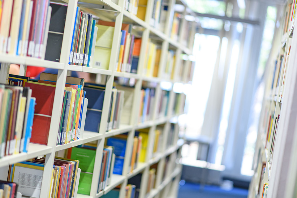 Helle Bibliothekregale mit vielen bunten Büchern.