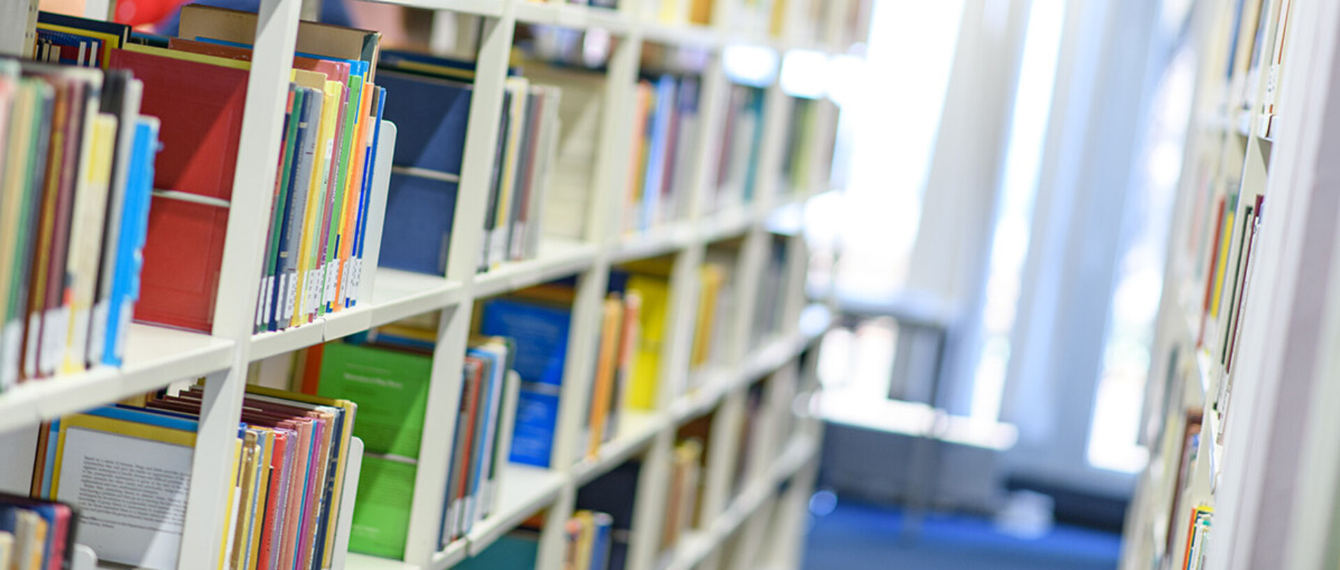 Helle Bibliothekregale mit vielen bunten Büchern.