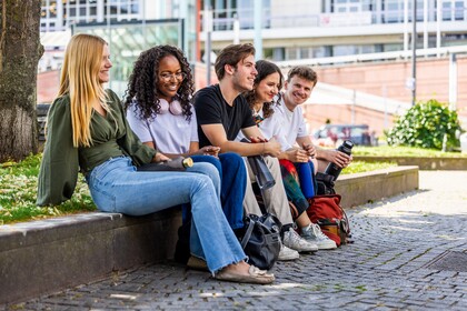 Fünd Studierende sitzen nebeneinander auf einer niedrigen Mauer.