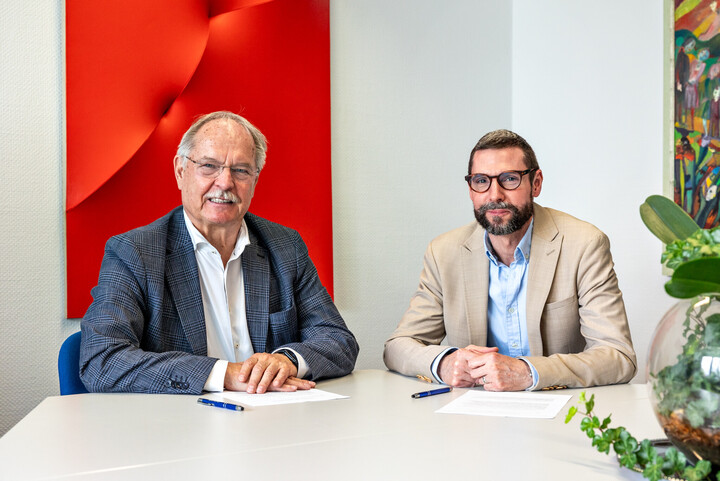 Dr. Peter Merten und Christian Haas sitzen an einem Tisch. Sie schauen in die Kamera. Vor ihnen liegen Zettel.