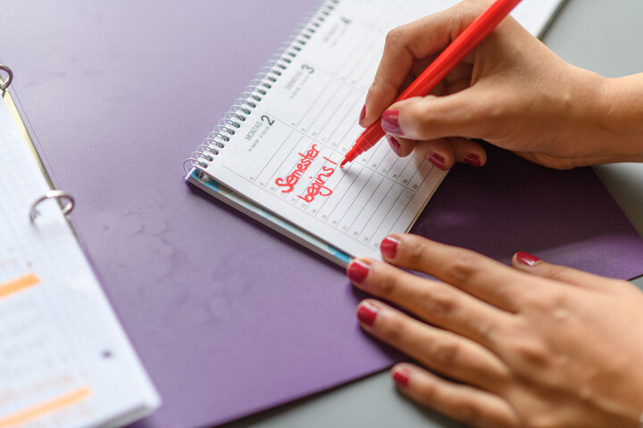 Eine Person schreibt mit Rotstift "Semester begins!" in einen Kalender.