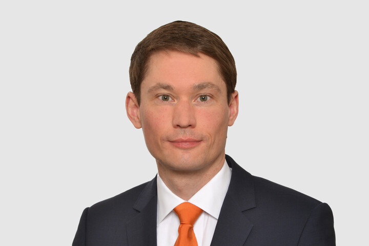 Prof. Bode hat kurze dunkle Haare und trägt ein weißes Hemd, ein dunkles Jacket und eine orangene Krawatte.