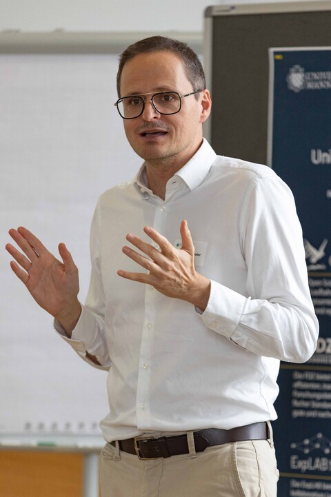 Prof. Strohmaier steht vor einem Whiteboard und hält einen Vortrag. Er trägt ein weißes Hemd und eine Brille.