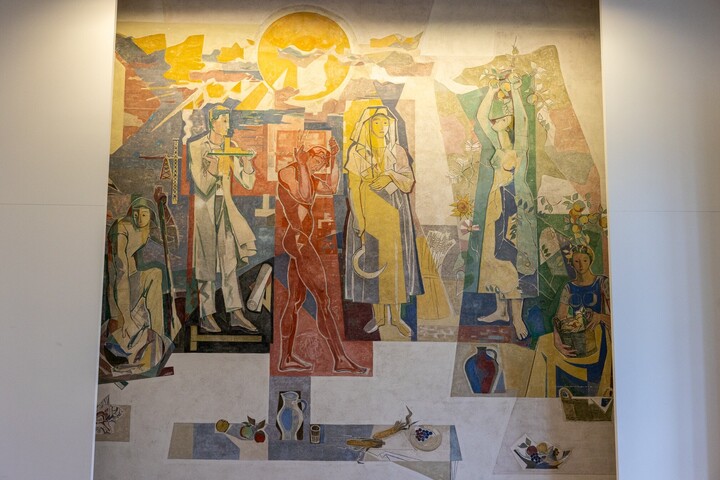 Buntes Wandbild: Im Mittelpunkt stehen sechs Personen in verschiedenen Posen. Über ihnen ist eine Sonne, unter ihnen ein gedeckter Tisch.