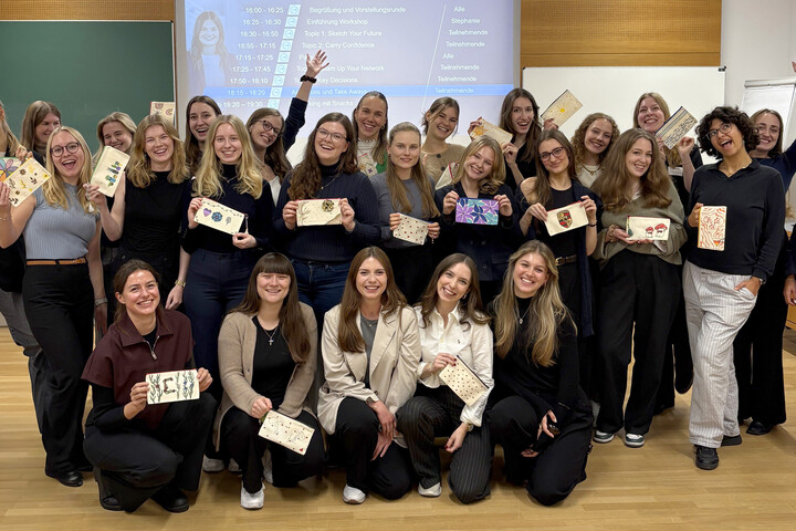 Eine Gruppe Frauen steht vor einer Powerpoint-Präsentation und jubelt.