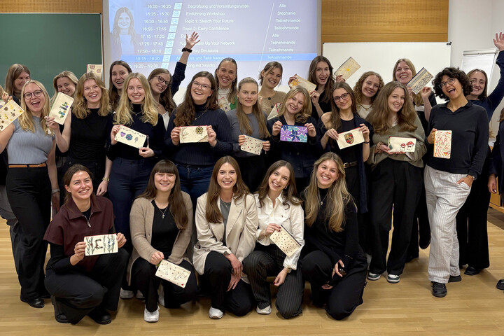 Eine Gruppe Frauen steht vor einer Powerpoint-Präsentation und jubelt.