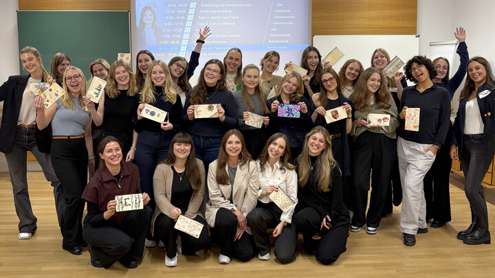 Eine Gruppe Frauen steht vor einer Powerpoint-Präsentation und jubelt.