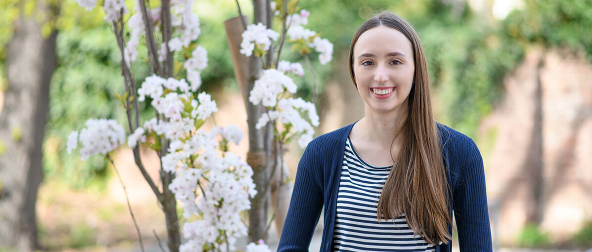 A young woman is smiling in front of a tree.