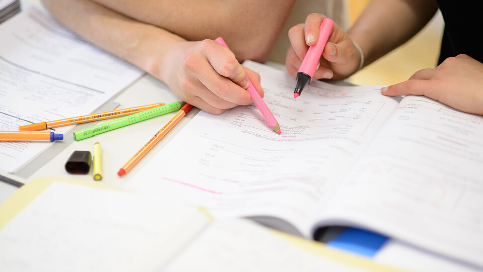 Zwei Studierende halten pinke Stifte in der Hand und zeigen sich etwas in einem Lernheft.