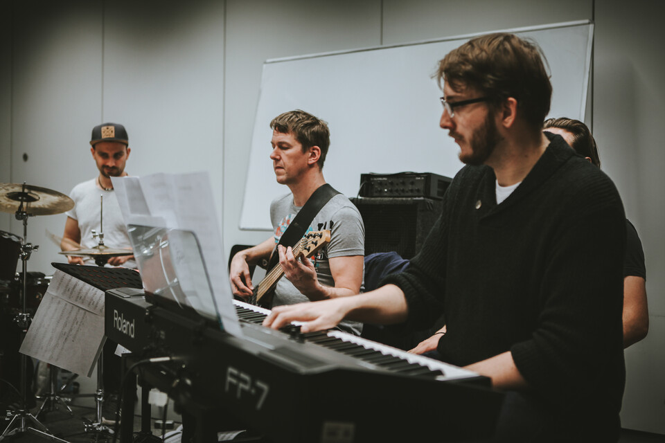Eine Person spielt Drums, eine Gitarre und eine andere Keyboard.