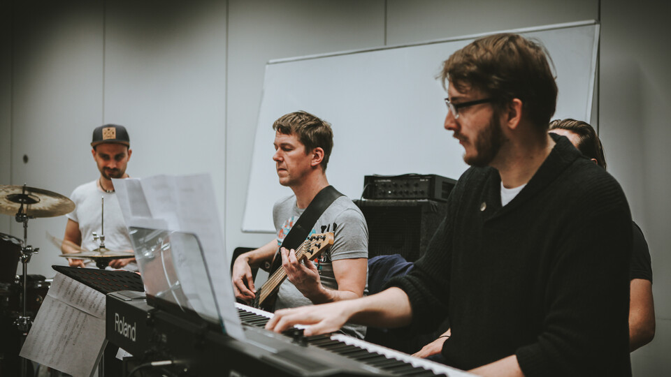 Eine Person spielt Drums, eine Gitarre und eine andere Keyboard.