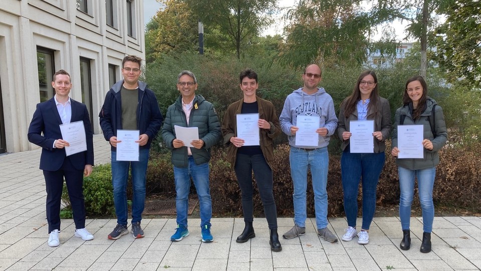 Seven people are standing in the courtyard of B6, 30-32 and are holding papers.