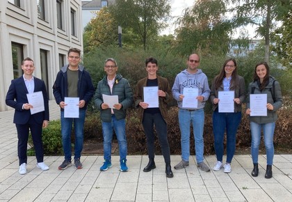 Seven people are standing in the courtyard of B6, 30-32 and are holding papers.