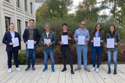 Seven people are standing in the courtyard of B6, 30-32 and are holding papers.