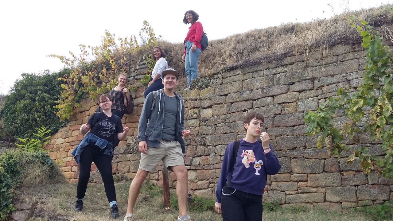 Studierende beim Wandern. Im Hintergrund stehen grüne Büsche und eine Steinmauer.