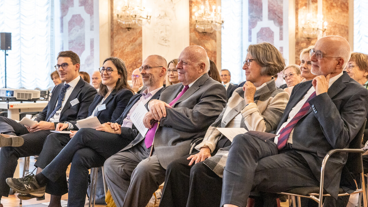 Mehrere Personen sitzen in einer Reihe auf Stühlen.
