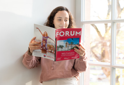 Eine Studentin lehnt an der Wand und liest das Magazin FORUM der Universität Mannheim.